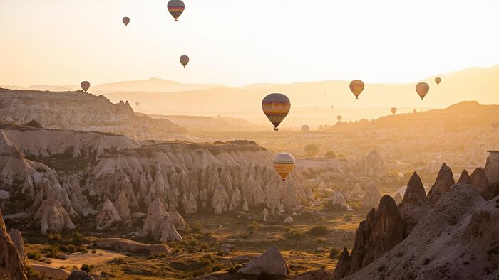 Fairy chimneys and valleys of Cappadocia in soft spring morning light, hot air balloons in a pale sky over the Central Anatolian plateau